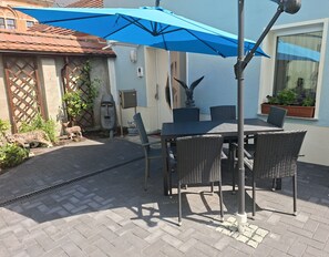 Une terrasse extérieure avec une table et des chaises, un parasol bleu et une statue représentant un visage.