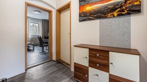 Ein Korridor mit einer Holztür, einer Kommode und einem Gemälde von einem Sonnenuntergang an der Wand.