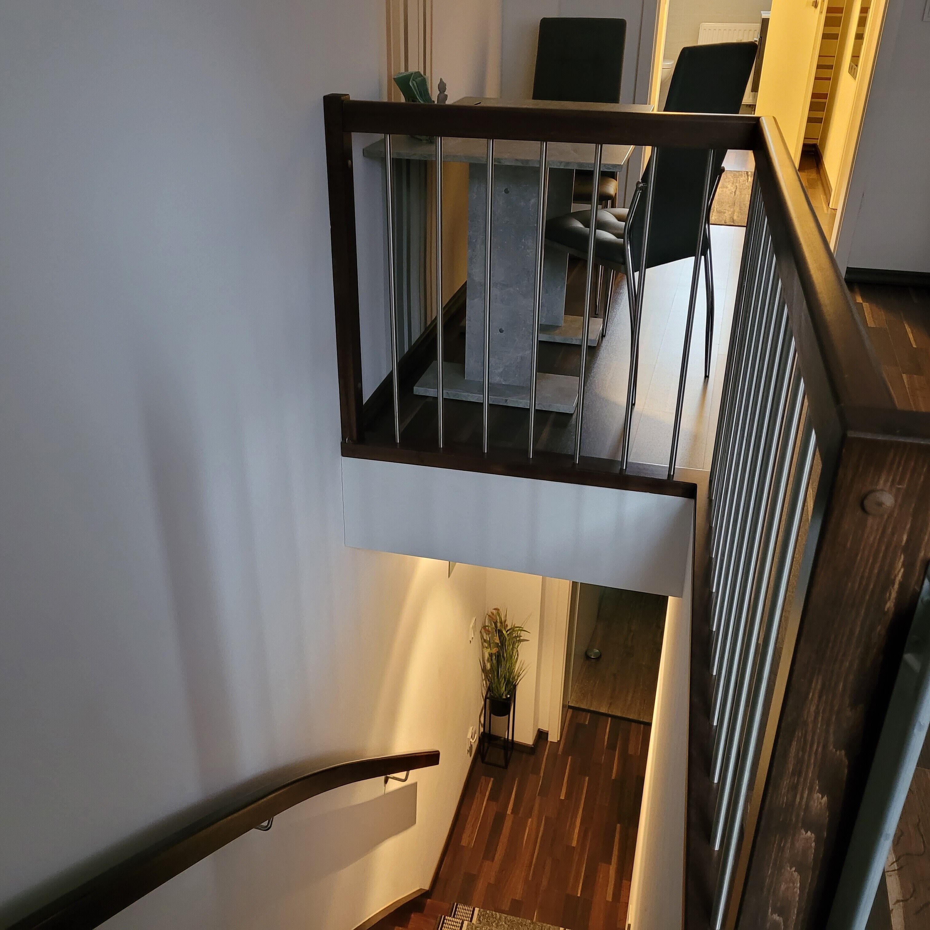 Een moderne trap met glazen leuning die leidt naar een eetruimte met een tafel en stoelen.