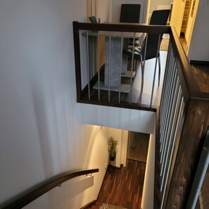 A modern staircase with a glass railing leading to a dining area with a table and chairs.