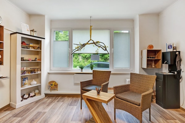 A room with a large window, wicker chairs, a wooden table, and a bookshelf.