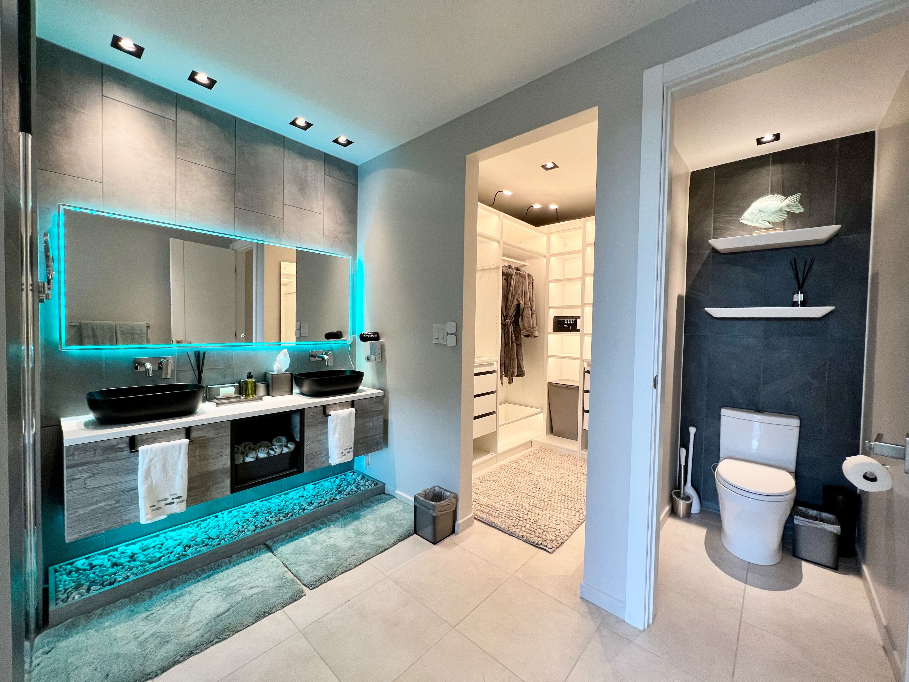 A modern bathroom with a large mirror, two sinks, a vanity, and a walk-in shower.
