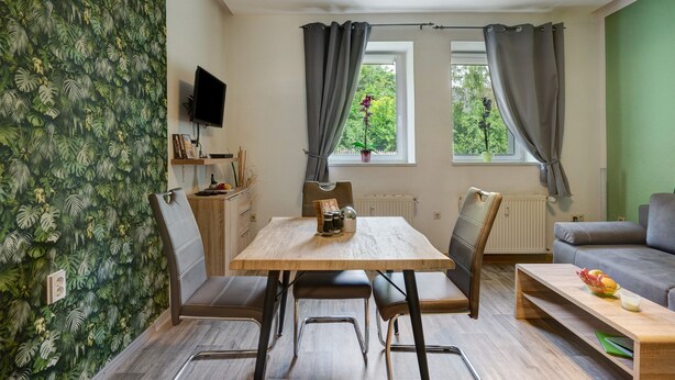 A room with a dining table, chairs, a sofa, a TV, and a window with curtains.