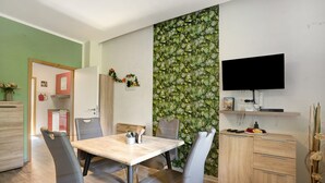 A dining area with a table, chairs, a TV, and a wall with a leafy pattern.
