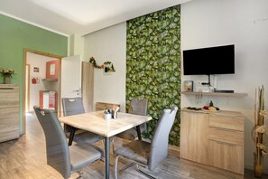 Un espace repas comprenant une table, des chaises, un téléviseur et un mur orné d’un motif végétal.