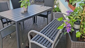 An outdoor patio with a table and chairs, a covered area, and potted plants.