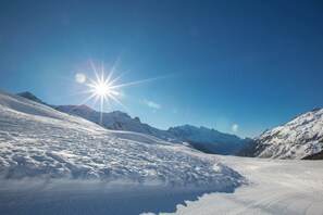 Paisaje nevado de montaña con cielo despejado y sol brillante.