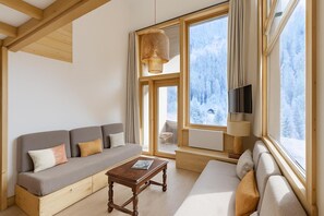 Een gezellige kamer met een bank, een kleine tafel, een televisie en grote ramen met uitzicht op een besneeerd landschap.