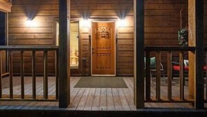 Una cabaña de madera con puerta principal, un porche con barandillas y un escalón que lleva a la puerta.