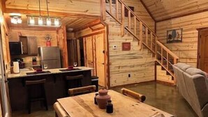 Interior de una cabaña de madera con cocina, comedor y una escalera.