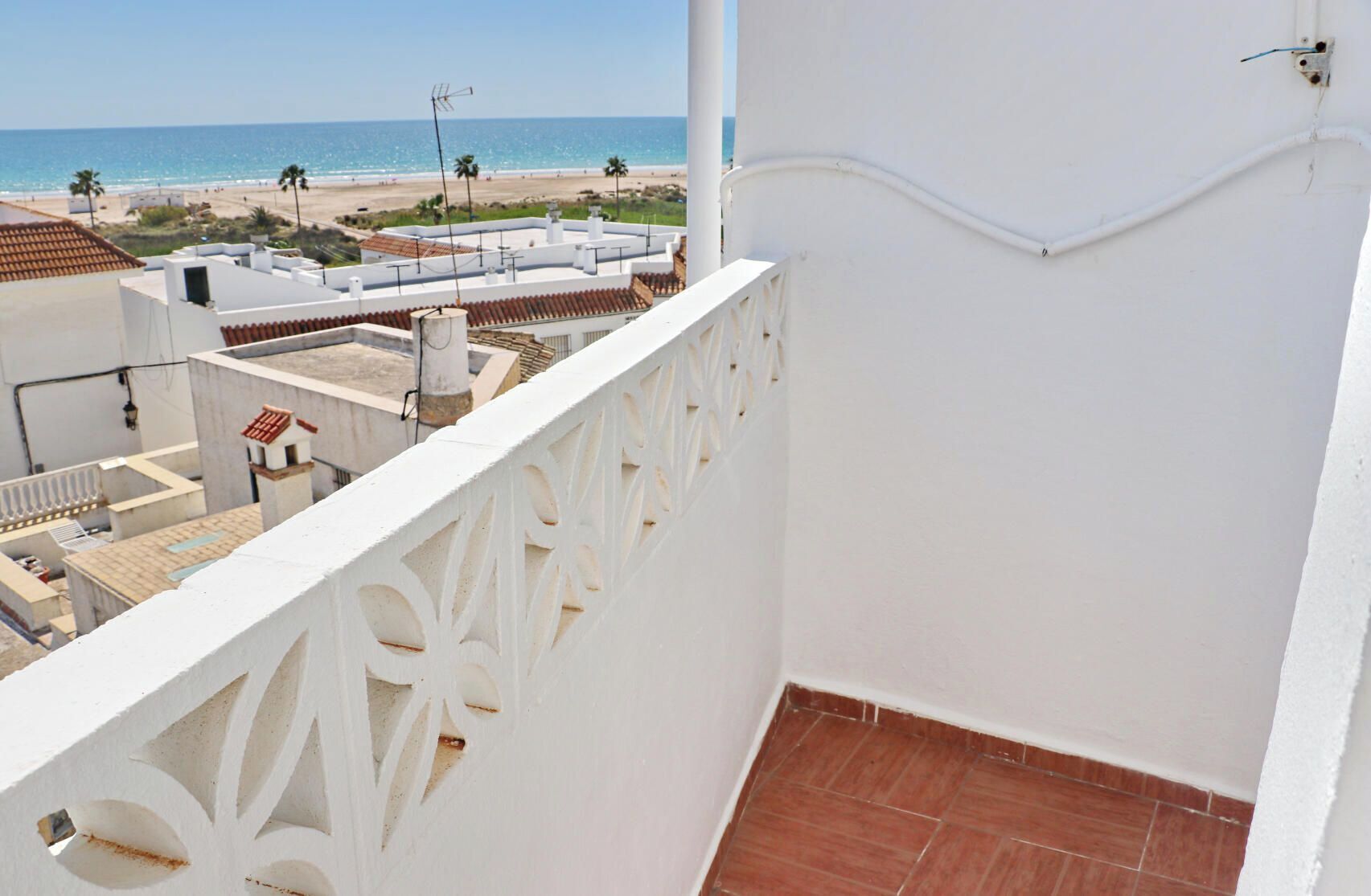 Un balcó amb barana blanca, vista a la platja i cel serè.
