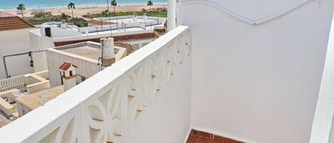 Un balcó amb barana blanca, vista a la platja i cel serè.