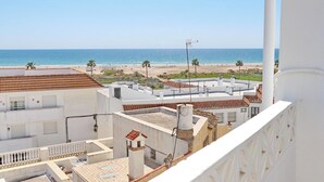 Vista costera desde un balcón con vistas a una playa, con edificios de techos rojos y paredes blancas.