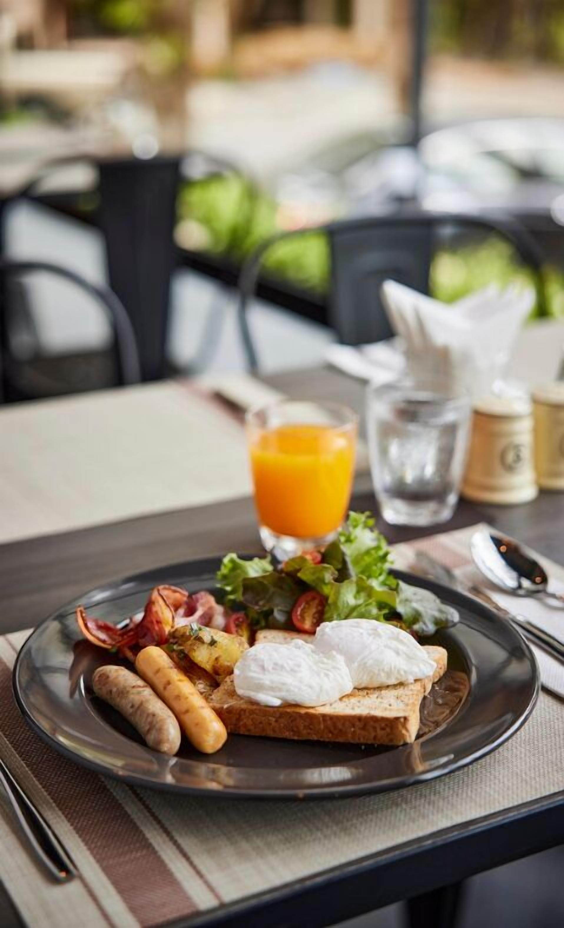 A breakfast plate with toast, eggs, sausages, and a salad, accompanied by a glass of orange juice and a water glass.