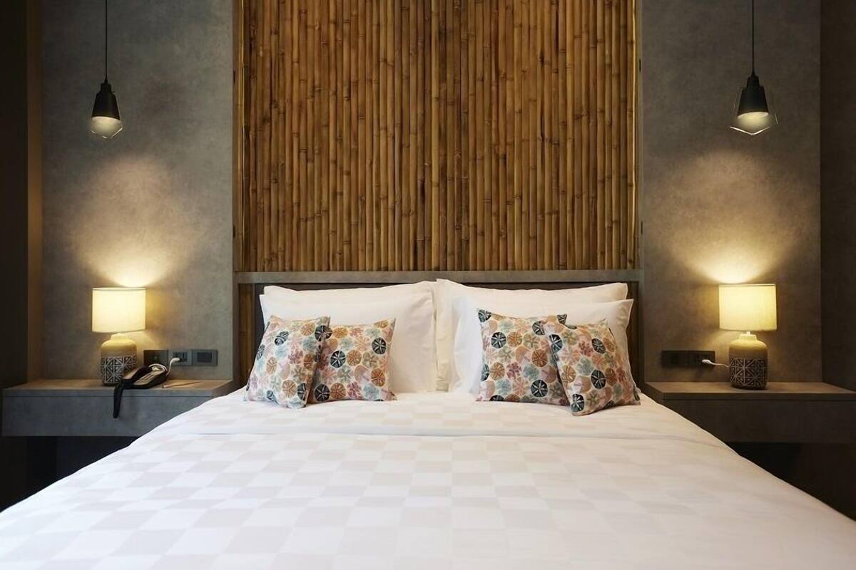 A modern hotel room with a large bed, two bedside lamps, and a wooden headboard.