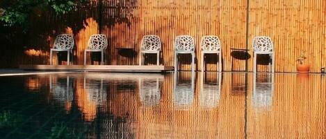 A pool area with six white chairs aligned against a bamboo wall.