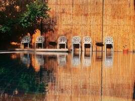 Un espace piscine avec six chaises blanches alignées contre un mur en bambou.