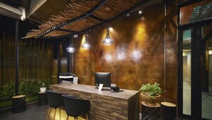 A modern reception desk with a wooden finish, black chairs, and pendant lighting. - Sand Dollar Boutique Hotel (Sattahip)