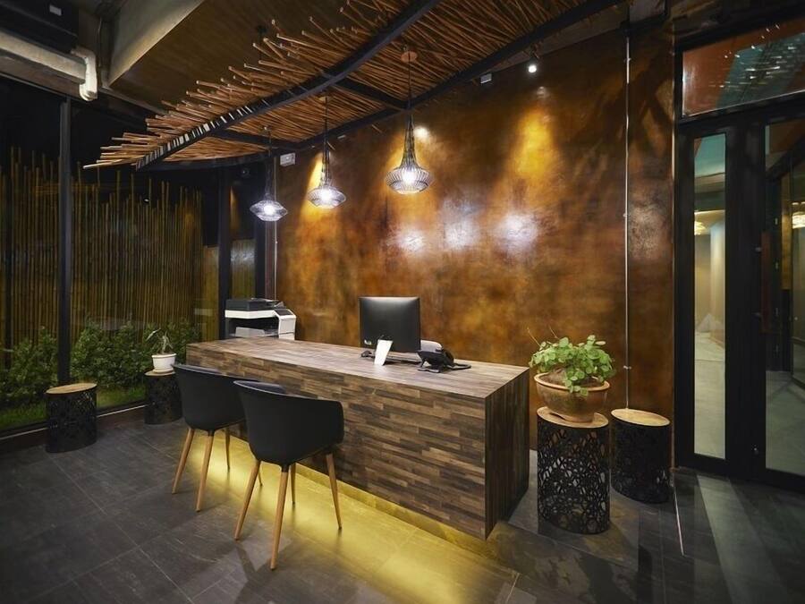 A modern reception desk with a wooden finish, black chairs, and pendant lighting.