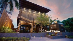 A modern building with a unique slatted roof design, surrounded by lush greenery and palm trees. - Sand Dollar Boutique Hotel (Sattahip)