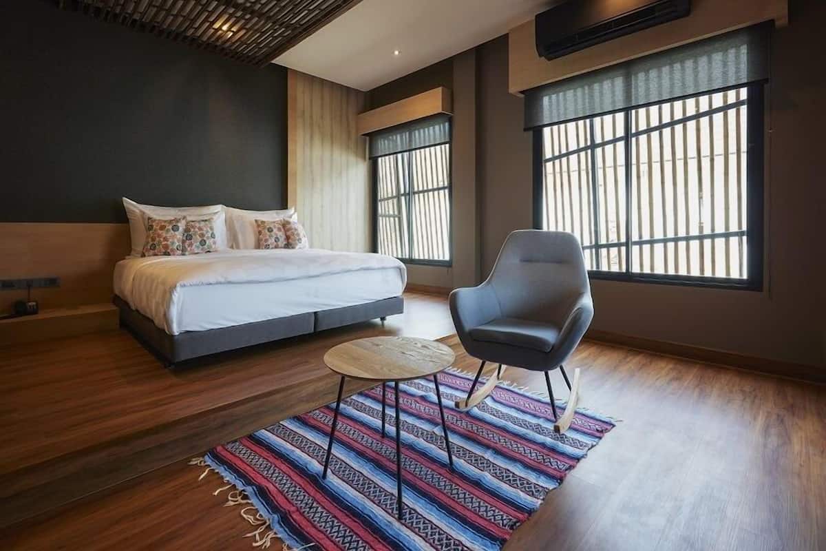 A modern bedroom with a large bed, a chair, a small round table, and large windows with bars.