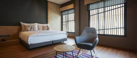 Un dormitorio moderno con una cama grande, una silla, una mesita redonda y ventanas amplias con barrotes.