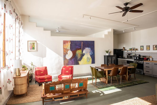 A spacious living area with a dining table, chairs, and a sofa. A kitchen is visible in the background with modern appliances.