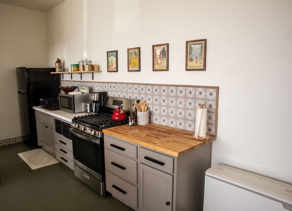 A kitchen with a stove, microwave, refrigerator, and a wooden countertop. There are four framed pictures on the wall above the countertop.