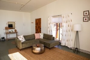 A living room with a sectional sofa, a round coffee table, a lamp, and a view through a window with curtains.