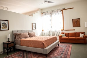 A bedroom with a bed, a nightstand, a sofa, and a window with curtains.