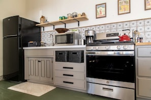 A compact kitchen with a black refrigerator, a microwave, a stove, and a toaster. There are cabinets with drawers and a small shelf above the counter.