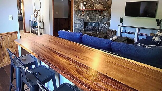 A modern living room with a wooden bar, blue sofas, and a stone fireplace. - 15 Fisher's Paradise on Lake Saluda w Boat Ramp (Greenville)