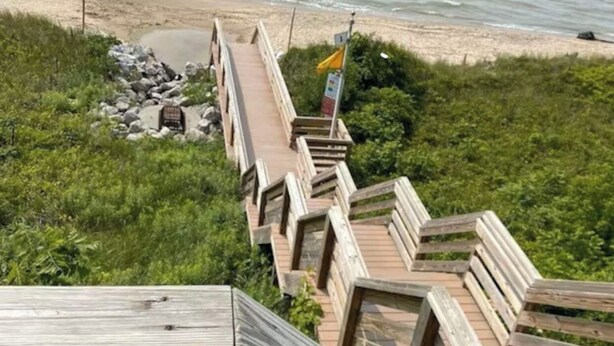 Une promenade en bois menant à une plage, avec un panneau indicateur et un drapeau.