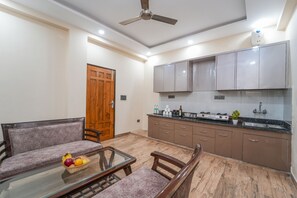 A modern kitchen with grey cabinets, a wooden door, and a dining area with a glass table and cushioned chairs.
