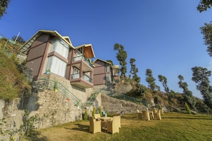 A hillside hotel with multiple balconies, outdoor seating, and a stone retaining wall.