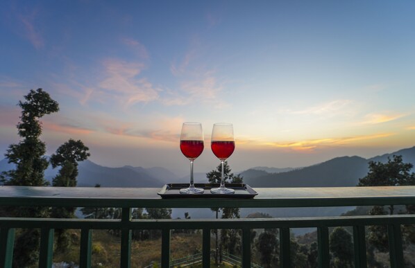 Two glasses of red wine on a tray with a scenic mountain view in the background.