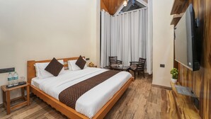Ein Hotelzimmer mit einem hölzernen Bett, einem Fernseher, einem kleinen Tisch mit Stühlen und einem Fenster mit Vorhängen.
