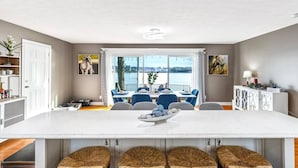 Een moderne eetruimte met een grote witte tafel, blauwe stoelen en uitzicht op het water.