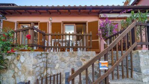 Una escalera de piedra conduce a una terraza de madera con mobiliario exterior, un muro de piedra y un cartel que dice 'AFFITTA'.