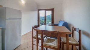 Una cocina compacta con refrigerador, una mesa de comedor con sillas y vistas al balcón a través de una puerta de cristal.