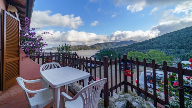Un balcón con mesa y sillas, con vistas panorámicas a un lago y montañas.