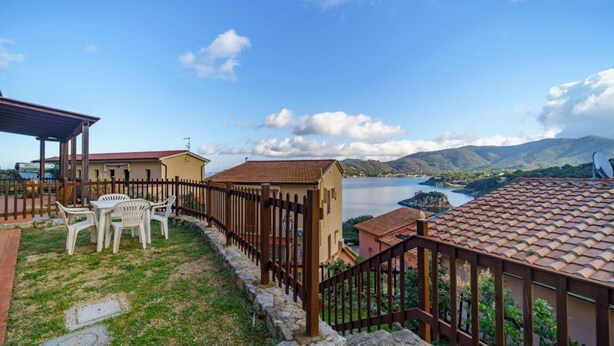 Una terraza con vistas a un lago y montañas, escalones de piedra y una valla de madera.