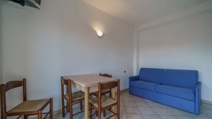 Una habitación con una mesa de comedor y cuatro sillas, un sofá azul y una lámpara fijada a la pared.
