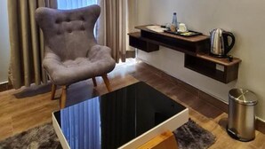 Una sala de estar moderna con un sillón capitoné, una mesa de centro de vidrio, un televisor de pantalla plana montado en la pared, una mesita auxiliar con una tetera y un cubo de basura.