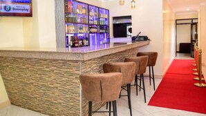 Zona de bar con mostrador de piedra, taburetes y una alfombra roja que conduce a una puerta.