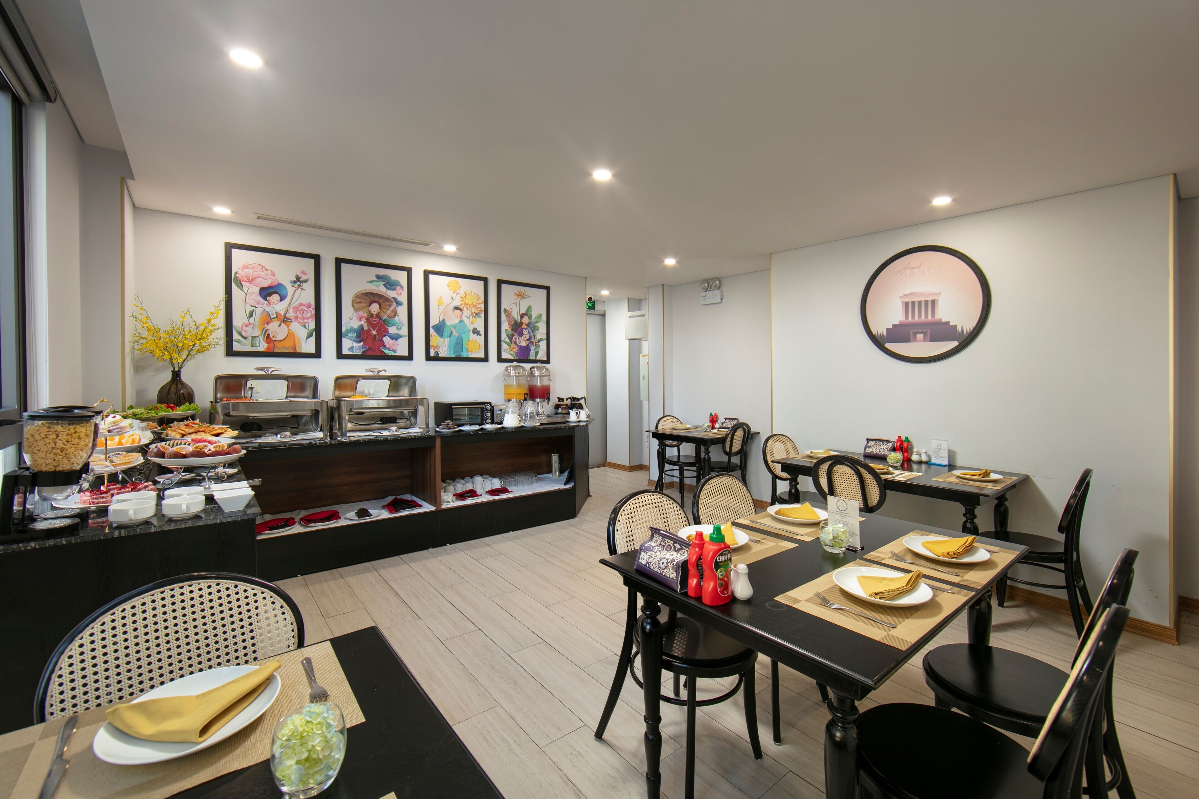Un espace de restauration d'hôtel avec un buffet, des tables, des chaises et des œuvres d'art accrochées aux murs.