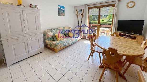 Ein Wohnzimmer mit Sofa, Esstisch, Fernseher und Schrank.