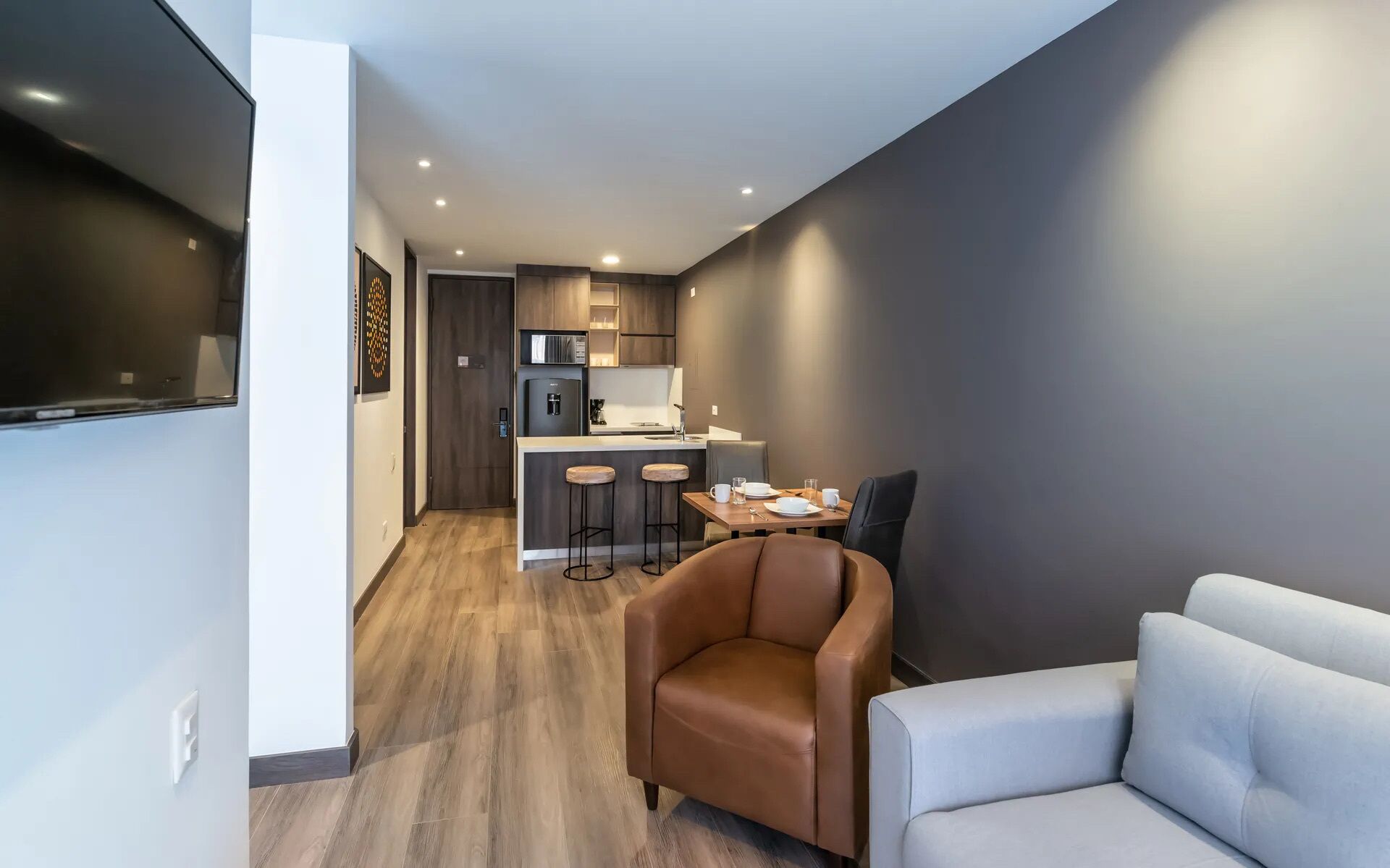 Una sala moderna con un sofá, un sillón y una zona de comedor con una mesa y taburetes.