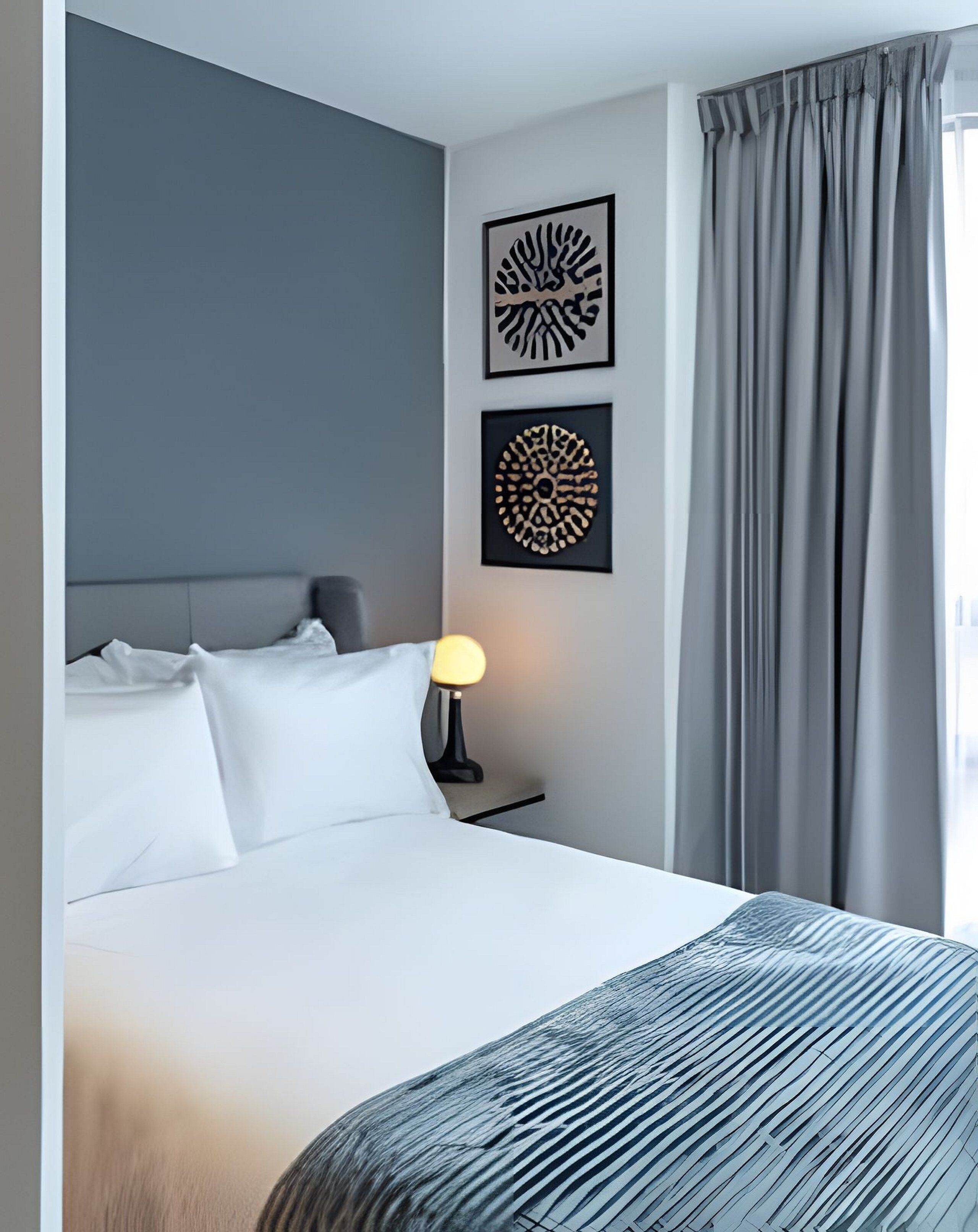 Et hotelværelse med en seng, et natbord med en lampe og to billeder på væggen.