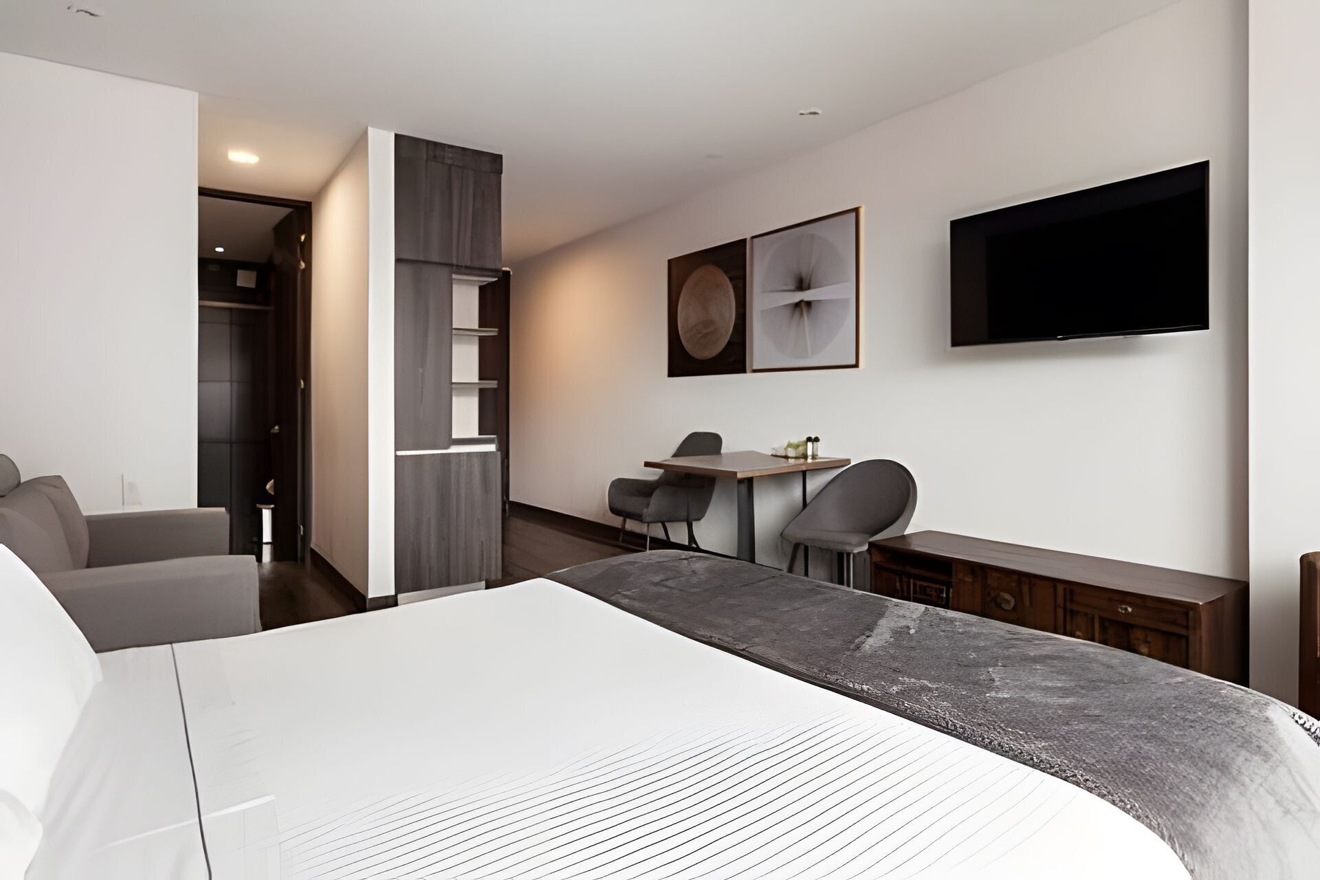 Een moderne hotelkamer met een groot bed, een bureau met twee stoelen, een aan de muur bevestigde televisie en een kledingkast met een inbouwkast.
